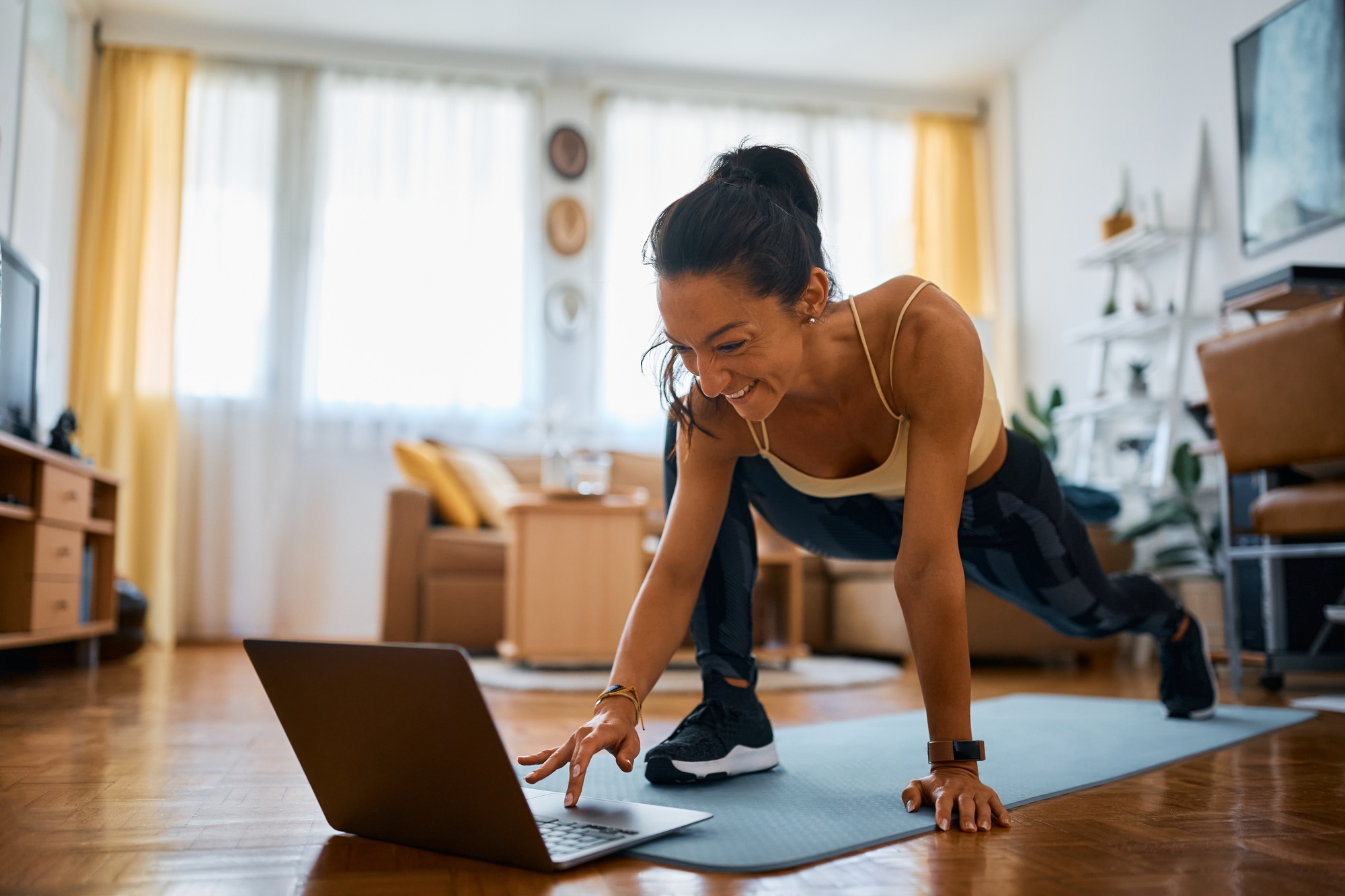 Happy fitness instructor using laptop while working out in the living room.