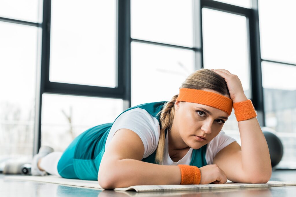 sad overweight girl lying on fitness mat in gym